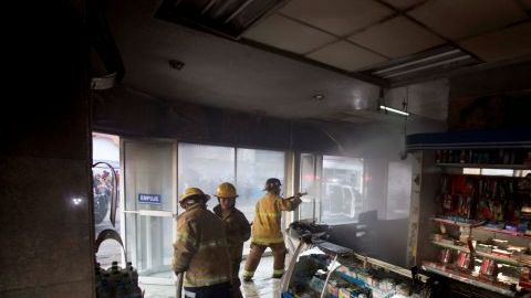 Bomberos realizan labores en una farmacia quemada en Apatzingán.