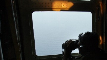 Un oficial de las fuerzas aéreas de Malasia busca en el mar los escombros del avion de la aerolínea de Malasia desaparecido.