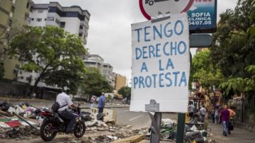 Transeúntes caminan junto a una barricada hecha con basura y escombros en las calles del sector El Cafetal, en Caracas.