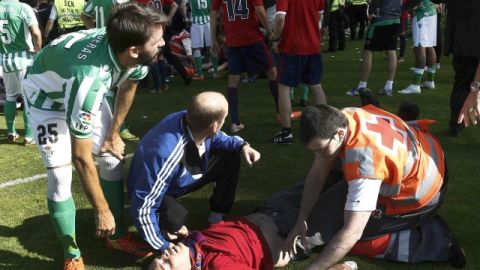 Un miembro de la Cruz Roja junto al defensa del Betis, Jordi Figueras (izq.), ayudan a uno de los heridos en la avalancha, ayer.