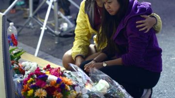Dos jóvenes arrodilladas luego de  colocar flores ante un altar que se levantó cerca al deli donde murió una de las víctimas del asesinato masivo del sábado.