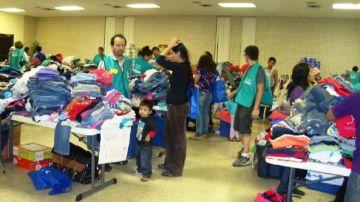 Voluntarios ayudan a inmigrantes a buscar ropa en el centro de acopio de Caridades Católicas.