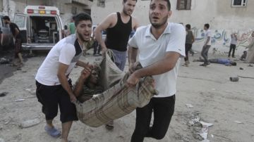 Unos hombres llevan en una manta a un joven palestino herido durante un bombardeo israelí sobre un mercado en la  ciudad de Gaza. La ONU y EEUU anunciaron que habrá 72 horas de tregua.