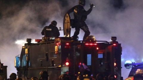 Un agente policíaco de Ferguson apunta a la multitud de protestantes con botes de gas lacrimógeno en la mano.
