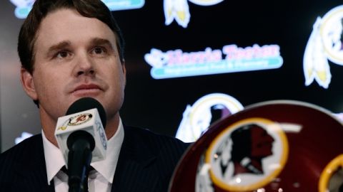 El coach de los Redskins, Jay Gruden, junto a un logo que podría desaparecer en la próxima temporada del fútbol americano profesional.