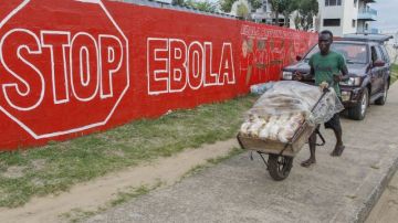 Un hombre lleva pan junto a un muro en con un anuncio de la campaña crada para combatir el brote de ébola en África Occidental, en Monrovia, Liberia.