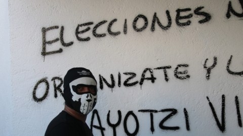 Un hombre encapuchado hace una pintada en una pared, durante una nueva jornada de protestas en rechazo a la desaparición de 43 estudiantes en  Iguala.