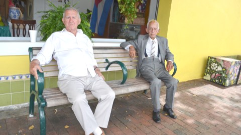 (Izq. a der.) Los cubanos René Herrera y Francisco Bijira sentados en una banca en las afueras del mercado frutería Pinareños.