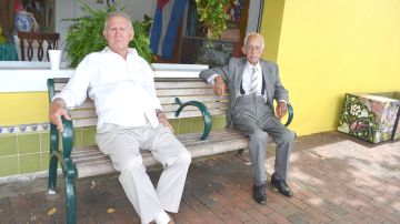 (Izq. a der.) Los cubanos René Herrera y Francisco Bijira sentados en una banca en las afueras del mercado frutería  Pinareños.