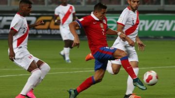 El futbolista chileno Alexis Sánchez anota un gol ante la marca de los peruanos Carlos Ascues  y Carlos Zambrano.