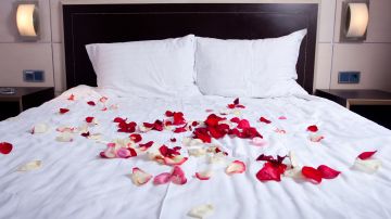 Adornar la cama vestida de blanco con pétalos de rosas rojas y rosadas invita a la pasión.