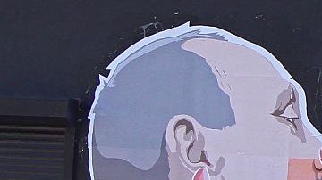 Una mujer pasa junto a un mural en un restaurante que representa al candidato presidencial Donald Trump y el presidente ruso, Vladimir Putin, que se saludan con un beso en Vilnius, Lituania.