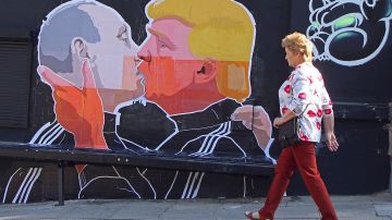 Una mujer pasa junto a un mural en un restaurante que representa al candidato presidencial Donald Trump y el presidente ruso, Vladimir Putin, que se saludan con un beso en Vilnius, Lituania.