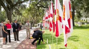 El gobernador de Florida, Rick Scott (d), deposita unas flores en las afueras del Capitolio Histórico en Tallahassee, cerca de una de las 49 banderas puestas como tributo a los muertos de la matanza en Orlando. Foto: EFE