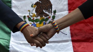 Miembros de la comunidad LGBT se dan la mano frente a una bandera de México.