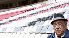 Melquiades Sánchez Orozco, la voz oficial del Estadio Azteca, posa con "Nachito", estatua localizada en uno de los asientos como monumento a los aficionados.