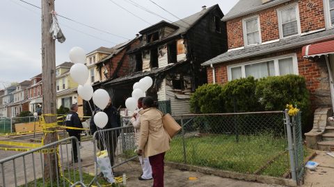 Debra Daniels y su amiga dejan globos y flores en la casa donde se produjo el fuego que mato a familia en Queens.