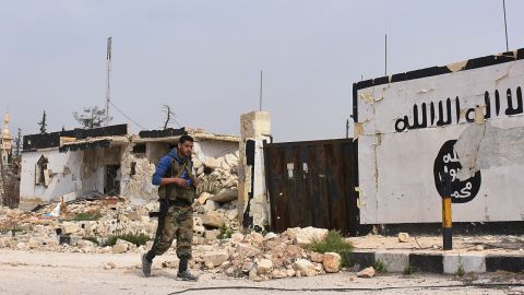 A member of the Syrian government forces walks past Islamic State (IS) group graffiti in Deir Hafer on the eastern outskirts of Aleppo on March 30, 2017, after they took control of the town from the jihadists. / AFP PHOTO / George OURFALIAN (Photo credit should read GEORGE OURFALIAN/AFP/Getty Images)
