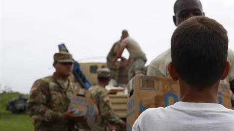 Un niño con una camiseta que lee 'Nunca nos quitamos' recibe una caja de alimentos entregada por miembros del Ejército en Las Piedras.
