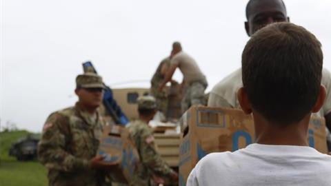 Un niño con una camiseta que lee 'Nunca nos quitamos' recibe una caja de alimentos entregada por miembros del Ejército en Las Piedras.