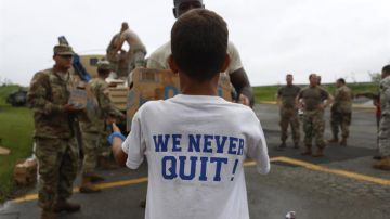 Un niño con una camiseta que lee 'Nunca nos quitamos' recibe una caja de alimentos entregada por miembros del Ejército en Las Piedras.