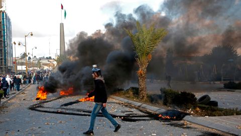 A Palestinian protester walks across a street riddled with stones during clashes with Israeli troops following a protest against US President Donald Trump's decision to recognize Jerusalem as the capital of Israel, near the Jewish settlement of Beit El, near the West Bank city of Ramallah, on December 7, 2017. / AFP PHOTO / ABBAS MOMANI