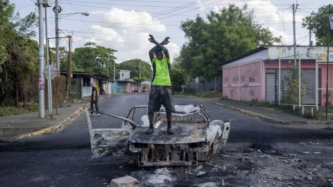 Un hombre protesta encima de un vehículo quemado.