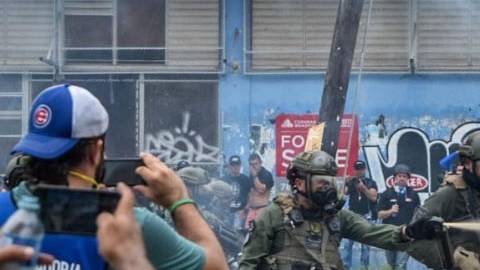 Agente  rocía con gas pimienta a una manifestante.