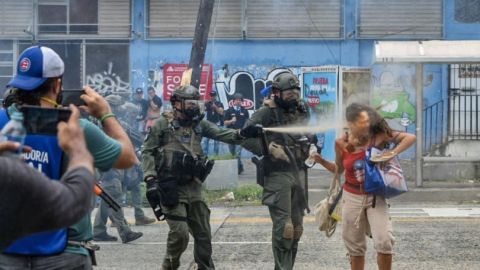 Agente rocía con gas pimienta a una manifestante.
