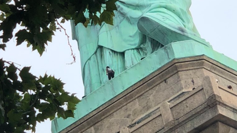 Una mujer intenta escalar la Estatua de la Libertad.