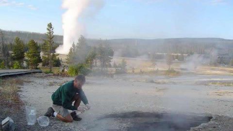 Un científico toma muestras en Ear Spring. Old Faithful se ve detrás.