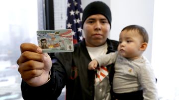 Luis Escamilla muestra su tarjeta de residente mientras carga a su hijo Jayden (Aurelia Ventura/La Opinion)