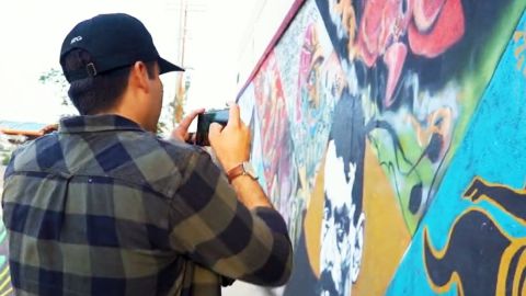 Esta imagen tomada de un video del sitio web latinx2.com muesta a un hobre fotografiando a un mural de arte hispano.