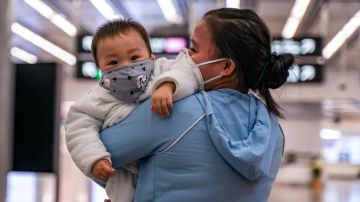 Una mujer lleva a un bebé con una máscara protectora en Hong Kong.