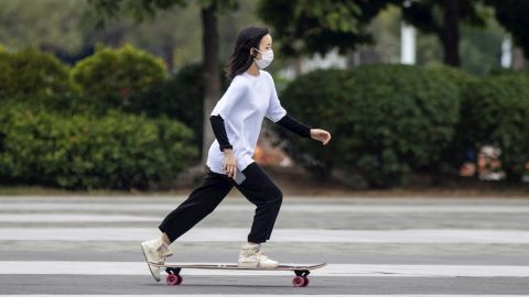 Una joven usa cubrebocas mientras monta en patineta en China.