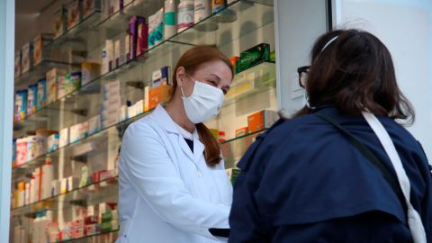 Una clienta conversa con una empleada a las puertas de una farmacia.