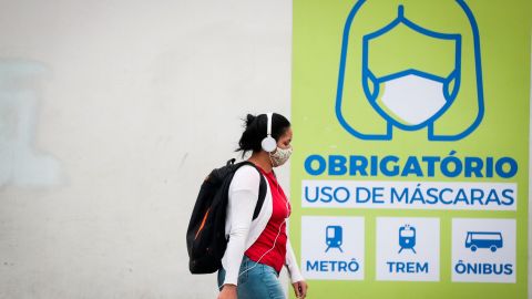 Una joven camina frente a un letrero que indica que el uso de la máscara es obligatorio en el transporte público en Sao Paulo.