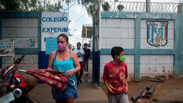 Una mujer junto a su hijo (d) utilizan tapabocas al salir de una escuela pública este viernes, en Managua.