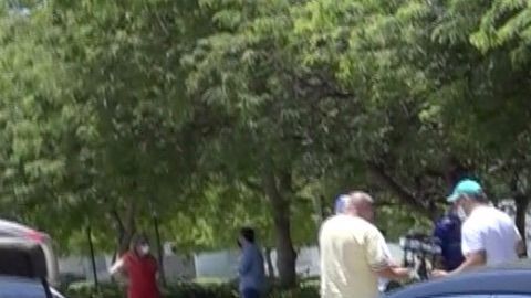 Una mujer deposita una bolsa con comida en un auto en Miami.