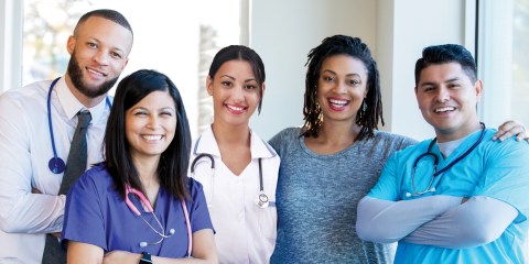 Diverse group of nurses, doctors, and other healthcare professionals are standing together confidently in a hospital hallway.