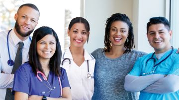 Diverse group of nurses, doctors, and other healthcare professionals are standing together confidently in a hospital hallway.