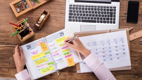 Close-up,Of,Businesswoman,Writing,Schedule,In,Calendar,Diary,On,Desk