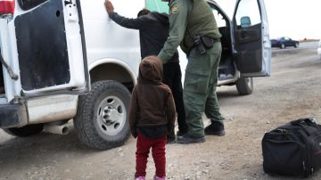 Un niño mira cómo un agente de la Patrulla Fronteriza revisa a un inmigrante.