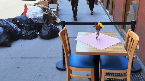 Acera compartida entre basura, peatones y comensales en NYC.