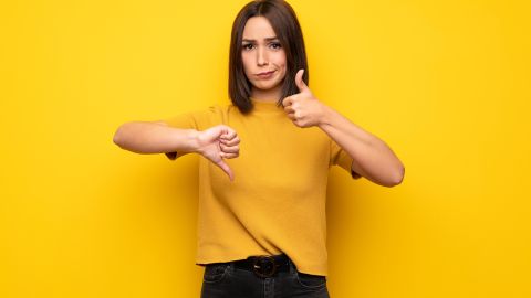 Young,Woman,Over,Yellow,Wall,Making,Good-bad,Sign.,Undecided,Between