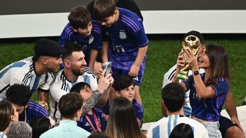 Antonela Roccuzzo (R) posa con la Copa del Mundo mientras su pareja, Lionel Messi, le toma una foto.