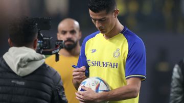 Cristiano Ronaldo firma un balón durante su presentación con el Al-Nassr.