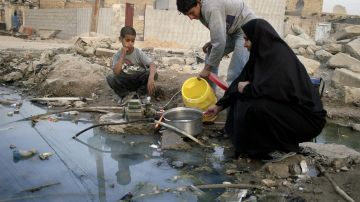 An Iraqi youth fills a pan with drinking