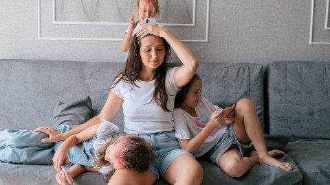 Tired,Young,Mother,Sits,On,Couch,And,Holds,Her,Head
