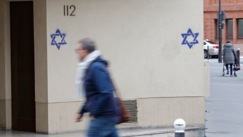Un hombre camina por un edificio cuya fachada está cubierta con estrellas de David pintadas durante la noche, en el distrito Alesia de París.